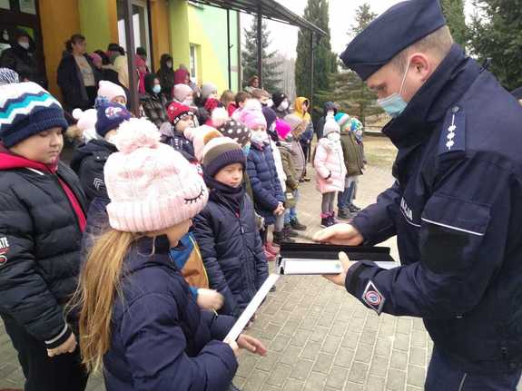 policjant dzielnicowy podczas rozdawania elementów odblaskowych dzieciom