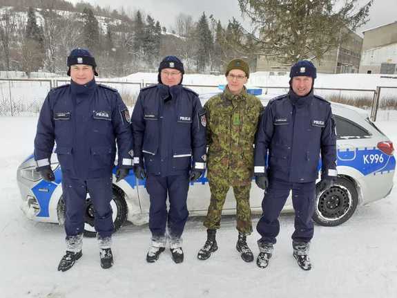 Na zdjęciu znajduje się czterech funkcjonariuszy, trzech umundurowanych policjantów oraz w kolejności trzeci od lewej funkcjonariusz Estońskiej policji w mundurze moro. Za nimi stoi radiowóz policyjny.