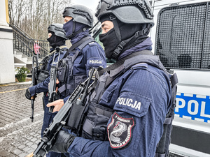 Trzech funkcjonariuszy Oddziału Prewencji Policji w Rzeszowie, w pełnym umundurowaniu, w hełmach i z bronią, na tle policyjnego radiowozu