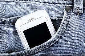 Zdjęcie kolorowe przedstawia telefon komórkowy koloru białego który umieszczony jest w kieszeni spodni.