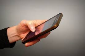 Zdjęcie kolorowe przedstawia telefon komórkowy kolory czarnego który jest trzymany w ręce kobiety.