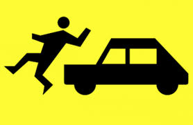 Zdjęcie przedstawia plakat na którym znajduje się samochód osobowy a przed nim osoba piesza . Plakat jest w kolorze żółtym a pojazd oraz osoba piesza jest w czarnym kolorze
