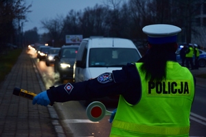 Policjantka zatrzymuje do kontroli kierowcę. Funkcjonariuszka w jednej ręce trzyma tarczę sygnalizacyją, a w drugiej urządzenie do sprawdzania stanu trzeźwości.