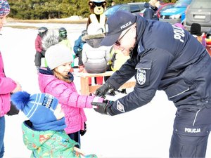 policjant zakłada na rękę małej dziewczynki opaskę odblaskową