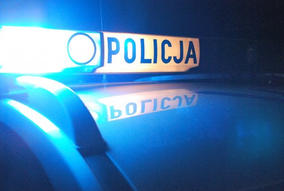 Belka policyjnego radiowozu z włączonymi światłami błyskowymi i napisem POLICJA