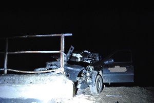 zdjęcie kolorowe wykonane w porze nocnej-przedstawia samochód osobowy m-ki volkswagen w granatowym kolorze. Pojazd brał udział w zdarzeniu drogowym jest rozbity, zaparkowany na barierze ochronnej mostu.