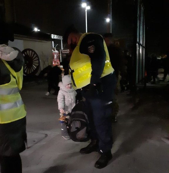 Policjant pomagający nieść bagaże dzieciom z Ukrainy