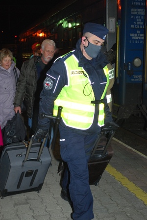 Zdjęcie kolorowe przedstawia policjanta który pomaga uchodźcom z Ukrainy  w przenoszeniu bagaży