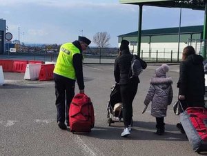 Zdjęcie kolorowe przedstawia policjanta który pomaga uchodźcom z Ukrainy  w przenoszeniu bagaży