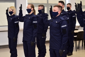 Nowo przyjęci policjanci podczas ślubowania, z podniesioną prawą ręką, stoją w maseczkach.