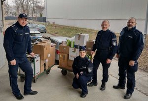 Na zdjęciu czworo umundurowanych policjantów z komisariatu na Baranówce, którzy przywieźli do magazynu zebrane dla uchodźców wsparcie. Za nimi spakowane w kartony dary.