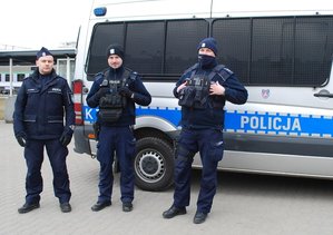 Na zdjęciu trzech umundurowanych policjantów przed dworcem PKP. Za policjantami stoi radiowóz.