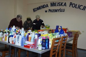 Zdjęcie kolorowe wykonane w porze dziennej -przedstawia pokój Komendy Miejskiej Policji w Przemyślu w którym są  składowane dary dla uchodźców z Ukrainy.