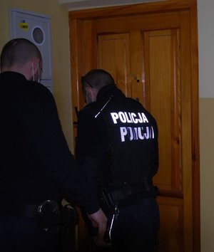 Dwóch policjantów stojących przy drzwiach mieszkania.