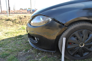 Zdjęcie kolorowe wykonane w porze dziennej –przedstawia lewy przedni bok pojazdu m-ki seat Leon w kolorze czarnym z uszkodzonym nadkolem. Pojazd brał udział w wypadku drogowym w miejscowości Żurawica