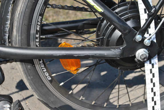 Zdjęcie kolorowe wykonane w porze dziennej –przedstawia tylne koło roweru w kolorze czarnym z uszkodzoną raną. Pojazd brał udział w wypadku drogowym w miejscowości Żurawica