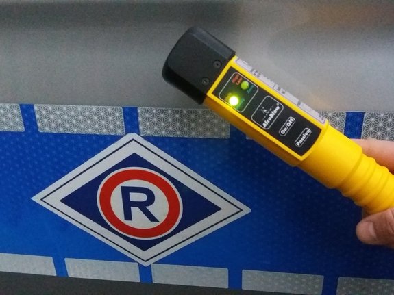 policyjne urządzenie do sprawdzania stanu trzeźwości z zapaloną zieloną diodą, na tle oznakowanego radiowozu ruchu drogowego