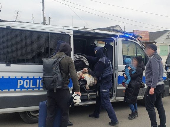 Zdjęcie kolorowe wykonane w porze nocnej -przedstawia granice polsko - ukraińska podczas trwania konfliktu zbrojnego na Ukrainie. Na pierwszym planie radiowóz w którym przebywają uchodźcy