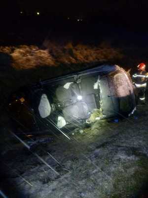 Zdjęcie kolorowe wykonane w porze nocnej-przedstawia samochód m-ki fiat stilo w kolorze granatowym. Samochód jest przewrócony na bok , obok pojazdu znajdują się strażacy