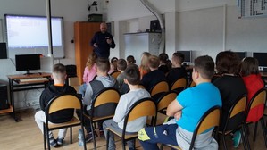 policjant w klasie podczas spotkania z uczniami, w tle wyświetlana prezentacja