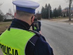 policjant ruchu drogowego w żółtej kamizelce wykonuje pomiar prędkości na drodze