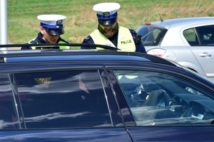 Dwaj policjanci ruchu drogowego w kamizelkach (po lewej) stoją przy czarnym samochodzie podczas kontroli stanu trzeźwości kierowcy.
