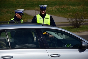 Dwaj policjanci ruchu drogowego w kamizelkach podczas kontroli stanu trzeźwości. Na pierwszym planie zatrzymany pojazd.