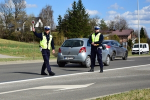 Dwaj policjanci ruchu drogowego w kamizelkach zatrzymują kierującego. W tle samochody.