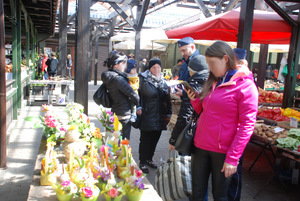 Zdjęcie kolorowe wykonane w porze dziennej przedstawia bazar warzywny przy ul. Sportowej w Przemyślu. W tle widoczni są dzielnicowi umundurowani , którzy podczas służby informują kupujących jak i sprzedających o zachowaniu ostrożności podczas zakupów przedświątecznych.