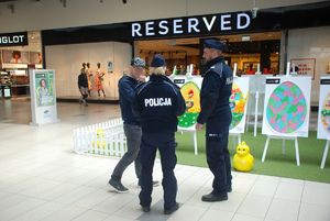 Zdjęcie kolorowe wykonane w porze dziennej przedstawia hol galerii „Sanowa” w Przemyślu. W tle widoczni są dzielnicowi umundurowani , którzy podczas służby informują kupujących jak i sprzedających o zachowaniu ostrożności podczas zakupów przedświątecznych.