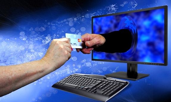 Zdjęcie przedstawia rękę wystającą z monitora. Ręką ta przekazuje kartę płatniczą ręce poza komputerem.