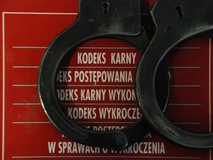 Kolorowa fotografia, zdjęcie przedstawiające policyjne kajdanki, leżące na czerwonym zbiorze kodeksów.