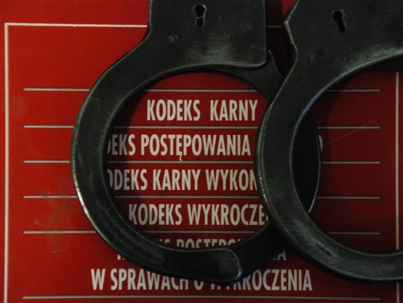 Kolorowa fotografia, zdjęcie przedstawiające policyjne kajdanki, leżące na czerwonym zbiorze kodeksów.