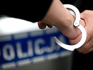 na zdjęciu policjant zakłada kajdanki na nadgarstek, w tle napis policja na radiowozie