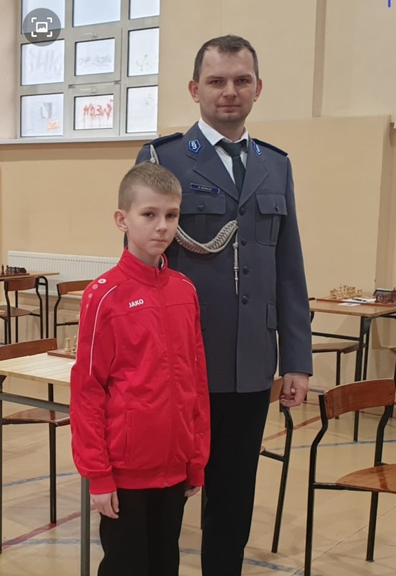 Policjant w mundurze po prawej, po lewej chłopiec w czerwonej bluzie sportowej.