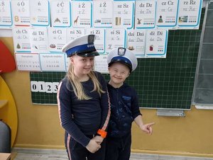Funkcjonariusze na spotkaniu z dziećmi w szkole. na zdjęciu dwoje dzieci w policyjnych czapkach