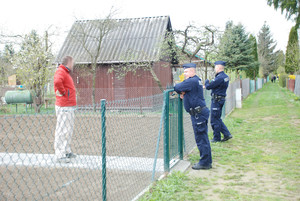 Zdjęcie kolorowe wykonane w porze dziennej -przedstawia ogródki działkowe na terenie miasta Przemyśl. Dwóch policjantów patroluje ogródki oraz rozmawia z działkowcami o bezpieczeństwie