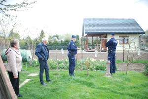 Zdjęcie kolorowe wykonane w porze dziennej -przedstawia ogródki działkowe na terenie miasta Przemyśl. Dwóch policjantów patroluje ogródki oraz rozmawia z działkowcami o bezpieczeństwie
