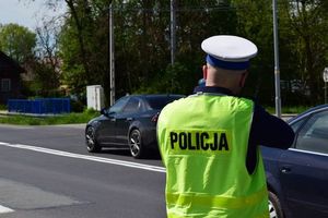 Zdjęcie kolorowe wykonane w porze dziennej -przedstawia policjanta ruchu drogowego który stoi na drodze z urządzeniem do pomiaru prędkości