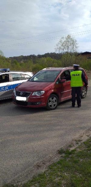 Na zdjęciu policjant ruchu drogowego, który sprawdza stan trzeźwości kierującego volkswagenem. Obok pojazdu stoi radiowóz policyjny.