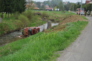 Zdjęcie kolorowe wykonane w porze dziennej –przedstawia samochód osobowy marki audi A$ w czerwonym kolorze, którym kierował nietrzeźwy kierowca. Kierujący stracił panowanie nad pojazdem i  wpadł do przydrożnego potoku