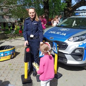 Na zdjęciu policjantka podczas pikniku w Strzyżowie pokazująca dziewczynce znak z &quot;autochodzika&quot; sygnalizacje swietlną - czerwone światło, obok radiowóz policyjny.