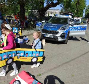 Na zdjęciu dzieci , które bawią się autochodzikiem, obok radiowóz policyjny