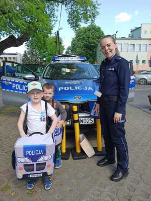 Na zdjęciu policjantka z dziecmi, które bawią się autochodzikiem - radiowozem policyjnym.