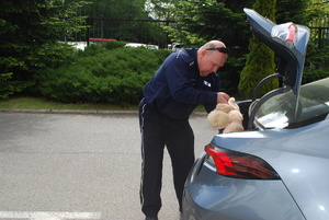 Zdjęcie przedstawia policjanta który wkłada do bagażnika samochodu misia