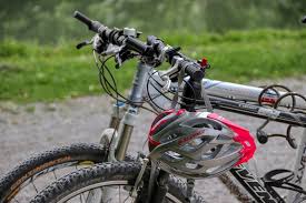 Zdjęcie kolorowe przedstawia dwa rowery jeden w kolorze czarnym , drugi srebrny na czarnym rowerze jest przewieszony kask rowerowy na kierownicy. Kask jest w srebrnym, na obrzeżach  ma kolor czerwony