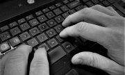 Fotografia przedstawia część klawiatury komputerowej oraz położone na niej dłonie. Fotografia czarno-biała.