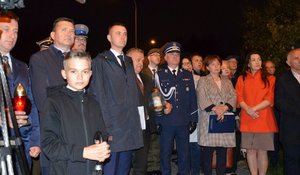 zdjęcie zbiorowe, na którym widać kilkanaście osób dorosłych, kobiet i mężczyzn, dwie z nich trzymają w rękach znicze, na pierwszym planie chłopiec. W centralnej części Komendant Wojewódzki Policji w Rzeszowie