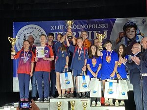 Na zdjęciu kilkanaście osób stojących na podium z medalami, dyplomami i pucharami za zdobycie trzech pierwszych miejsc w Ogólnopolskim Turnieju Bezpieczeństwa w Ruchu Drogowego. Za osobami wisi plakat turnieju.