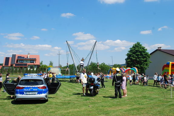 Zdjęcie ogólne, przedstawia uczestników pikniku. Na pierwszym planie widoczny policyjny radiowóz oraz motocykl. W oddali dzieci na trampolinie.